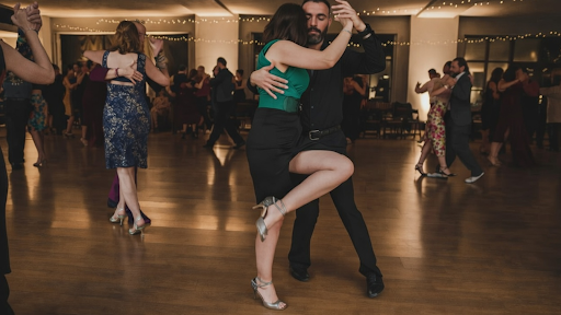 A couple performs a salsa dip on the dance floor with others under warm lights.