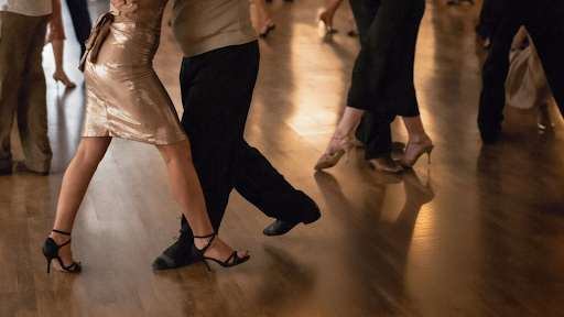 Feet dancing: crossed heels in skirt, forward step in black shoes.
