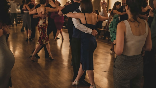 A group of people dancing closely together, with couples holding each other under soft lights.